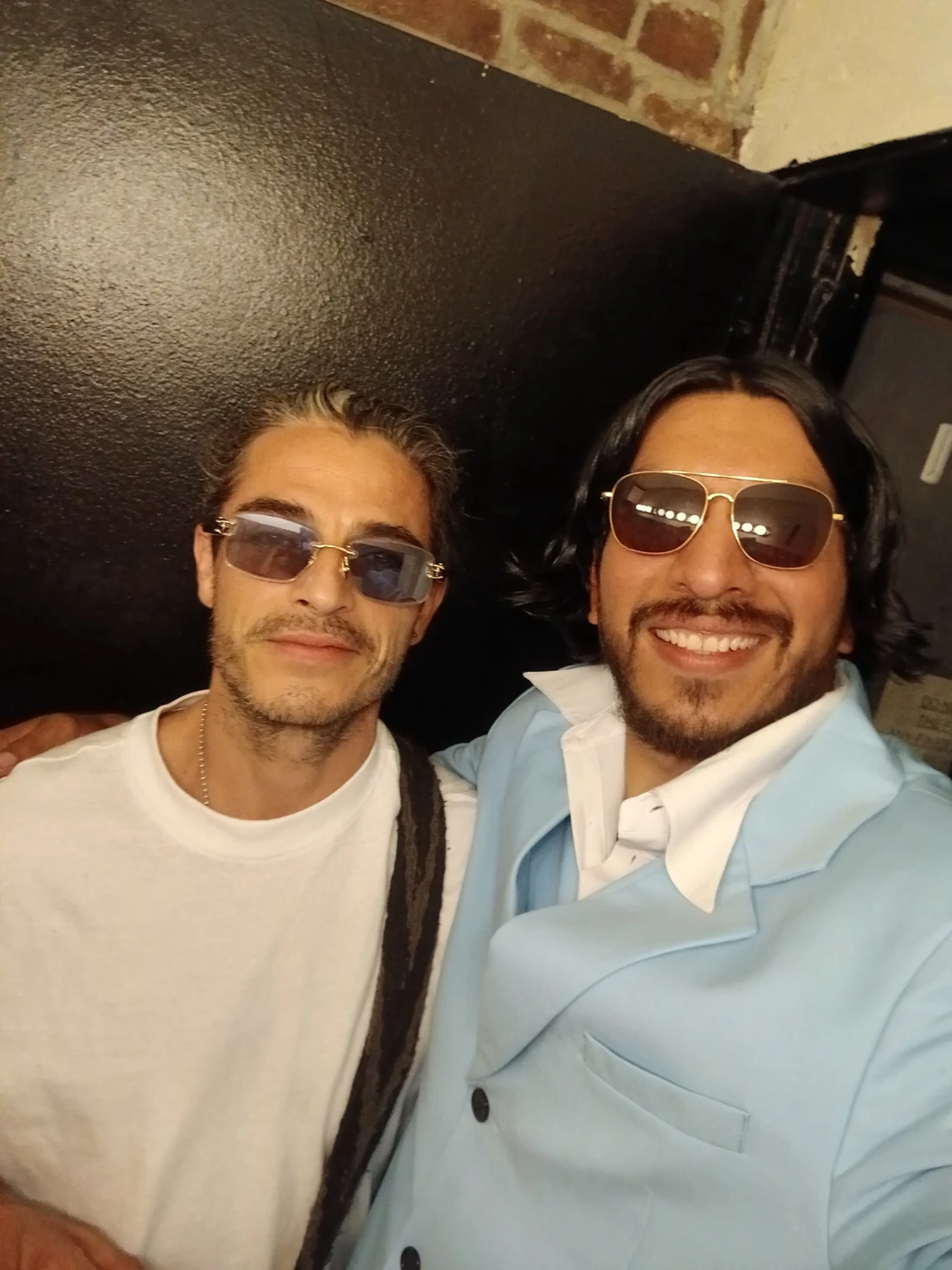 Francisco Yazbek in a light-blue suit and sunglasses posing with another man in a white shirt