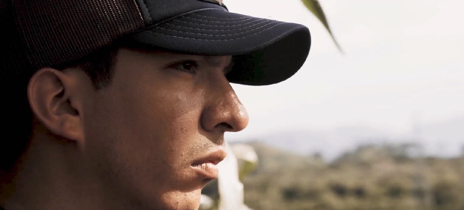 El Deportado production image: profile of a young man in a dark cap, looking across a sunlit landscape