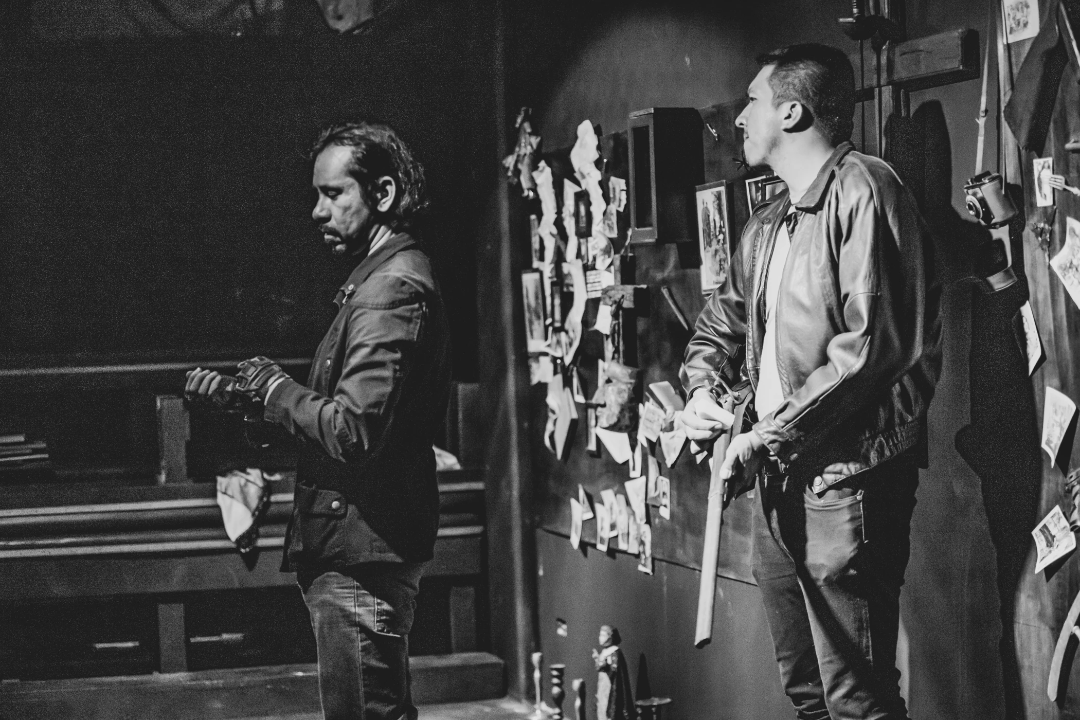 Two performers in a black-and-white theatre photograph, with a wall of photographs behind them